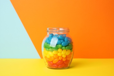 Photo of Jar of delicious jelly beans on color background. Space for text