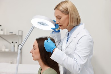 Photo of Trichologist examining patient`s hair under lamp in clinic