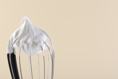 Photo of Whisk with whipped cream on beige background, closeup. Space for text