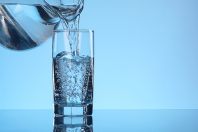 Photo of Pouring water from jug into glass on light blue background. Space for text