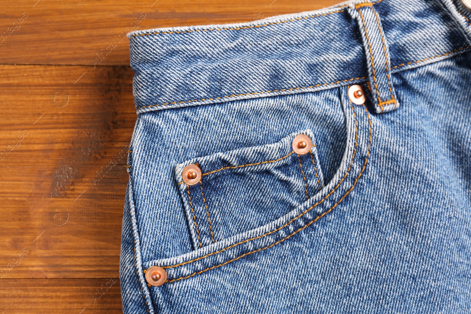 Photo of Stylish light blue jeans on wooden background, closeup of inset pocket