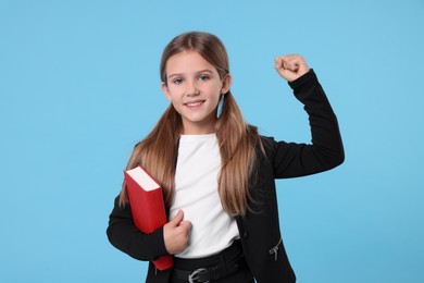 Happy schoolgirl with book on light blue background