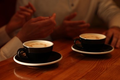 Photo of Couple with cups of aromatic coffee at wooden table, closeup