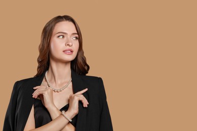 Photo of Young woman wearing elegant pearl jewelry on brown background, space for text