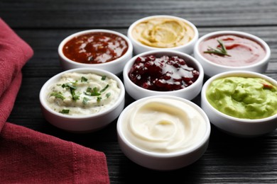 Different tasty sauces in bowls on black wooden table, closeup