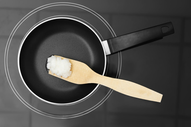 Photo of Frying pan with coconut oil and wooden spatula on induction stove, top view. Healthy cooking