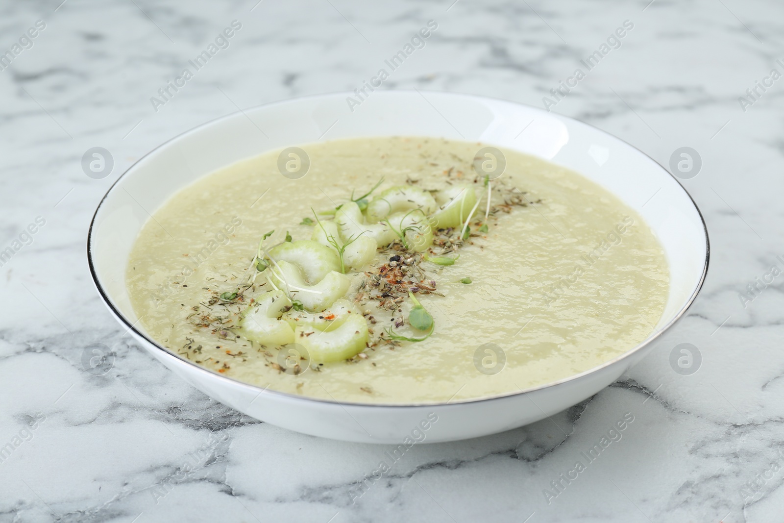 Photo of Bowl of delicious celery soup on white marble table