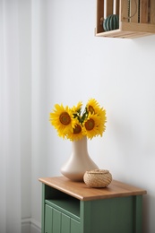 Photo of Bouquet of beautiful sunflowers and wicker basket on table indoors