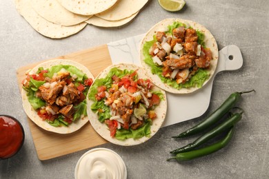 Photo of Delicious tacos with vegetables, meat and sauce on grey textured table, flat lay