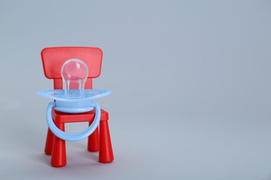 Maternity leave concept. Toy chair with baby pacifier on light grey background, space for text