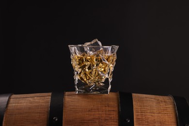 Whiskey in glass on wooden barrel against dark background