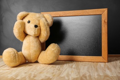 Photo of Teddy bear covering eye and small blackboard on wooden table. Space for text