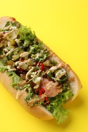 Photo of Delicious hot dog with chili peppers, lettuce, pickles and sauces on yellow background, closeup