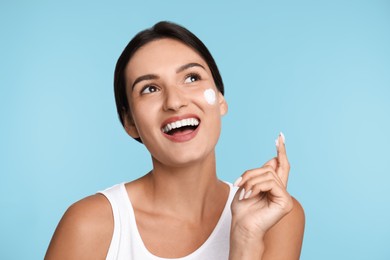 Photo of Young woman applying facial cream on light blue background