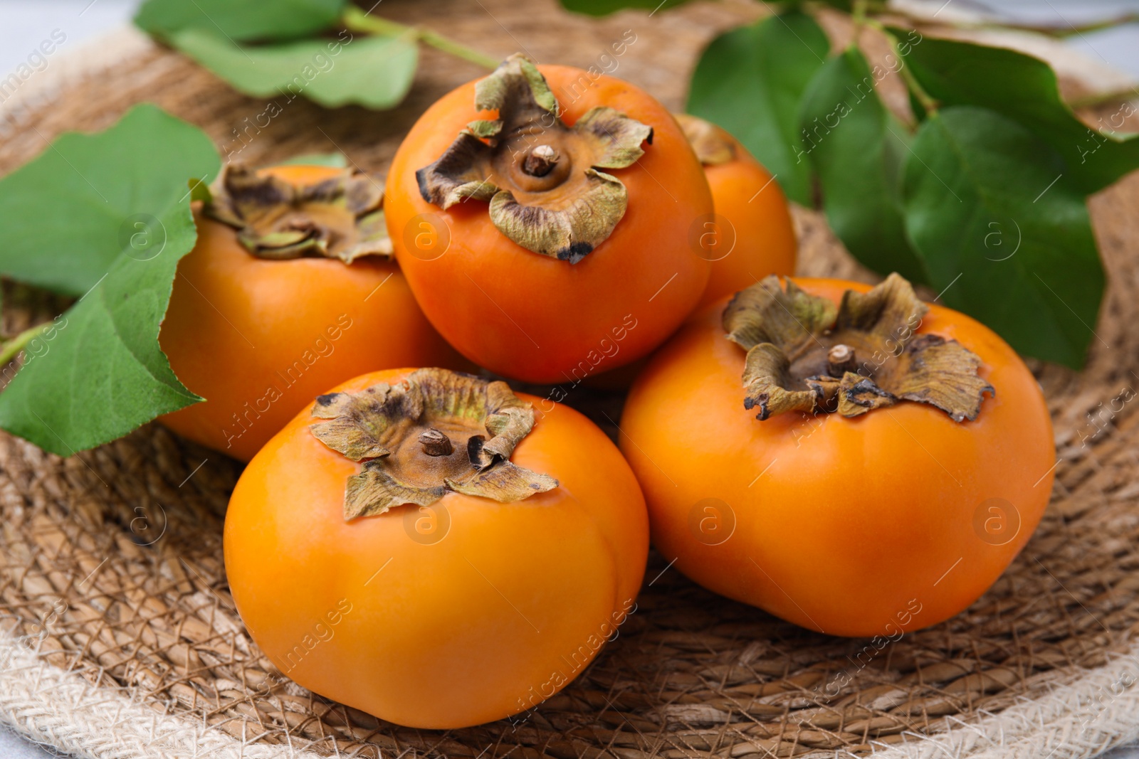 Photo of Delicious ripe juicy persimmons on wicker mat, closeup