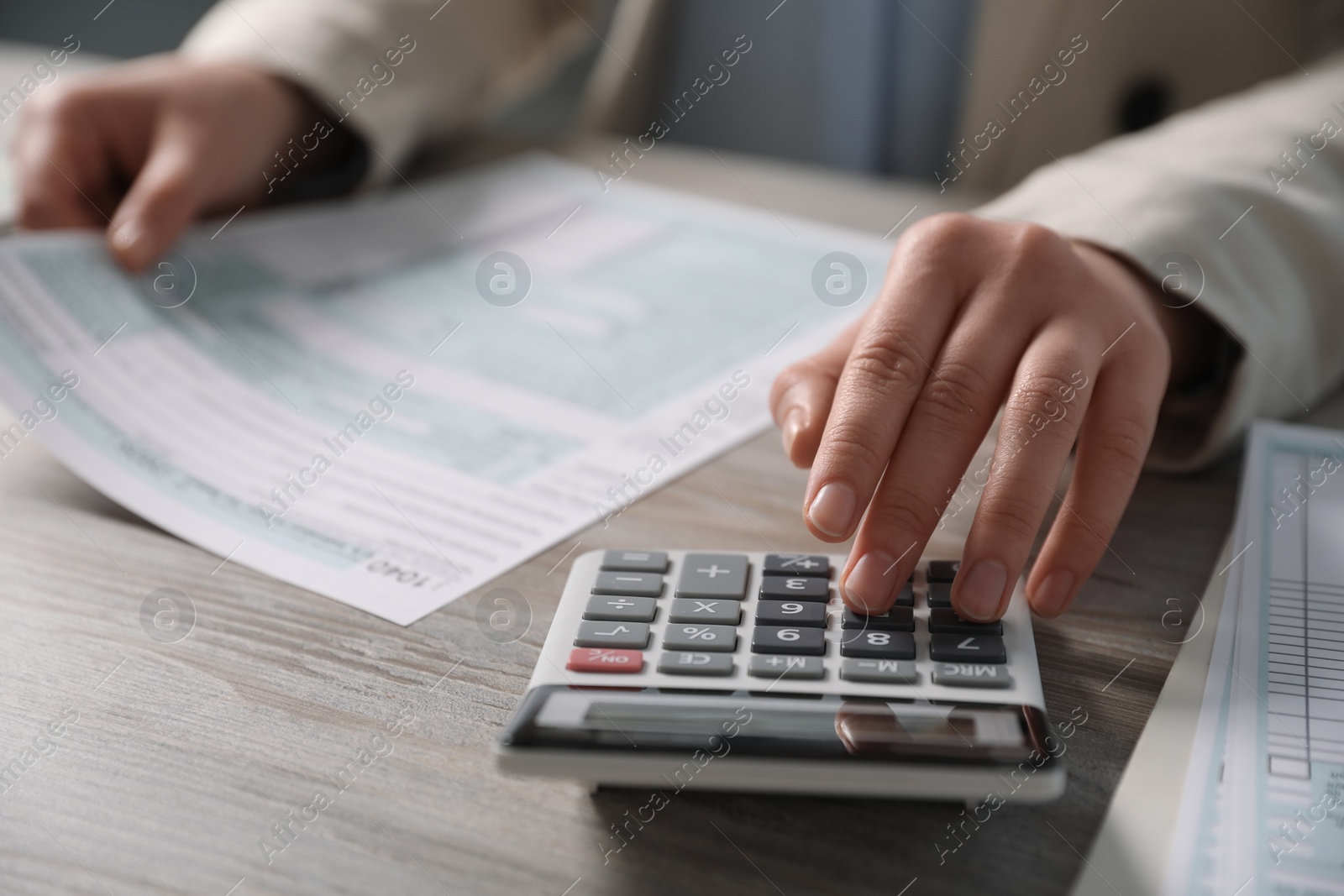 Photo of Payroll. Woman using calculator while working with tax return forms at wooden table, selective focus