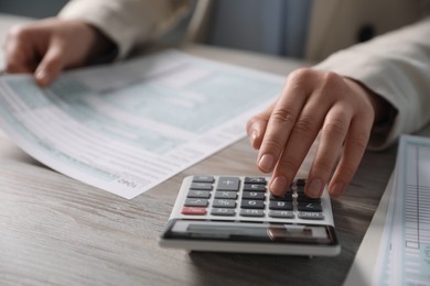 Photo of Payroll. Woman using calculator while working with tax return forms at wooden table, selective focus