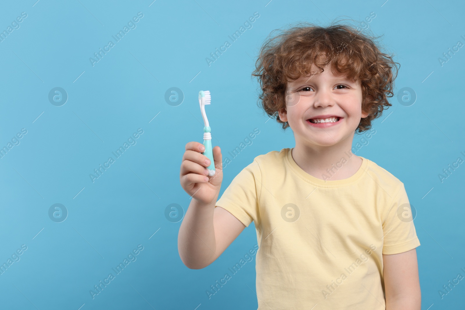 Photo of Cute little boy holding plastic toothbrush on light blue background, space for text