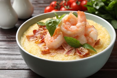 Photo of Fresh tasty shrimps, bacon, grits and basil in bowl on wooden table, closeup