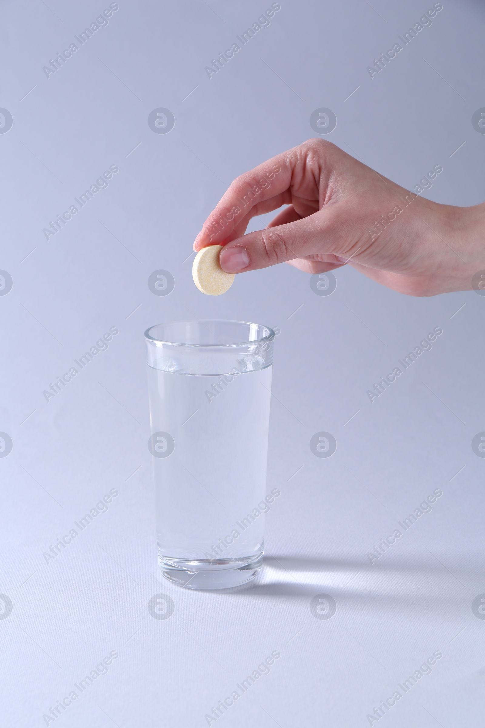 Photo of Woman putting effervescent pill into glass of water on light grey background, closeup