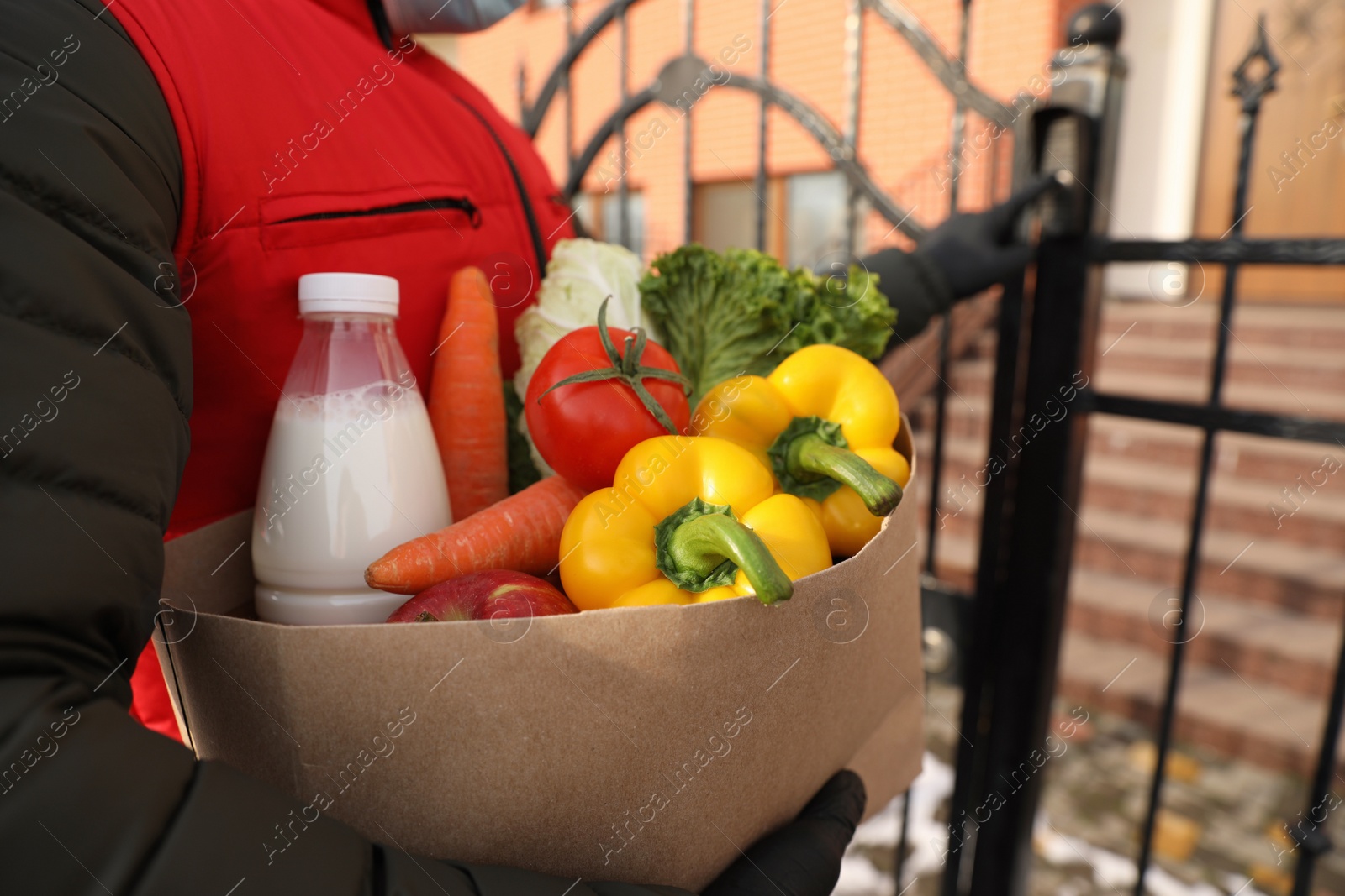 Photo of Closeup view of courier ringing gate bell outdoors, focus on paper bag with groceries. Delivery service during quarantine due to Covid-19 outbreak