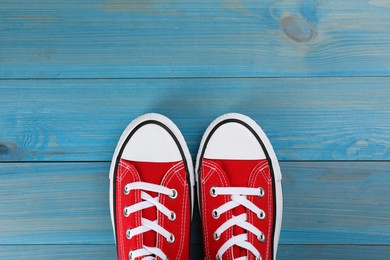 Photo of Pair of red sneakers on light blue wooden table, flat lay. Space for text