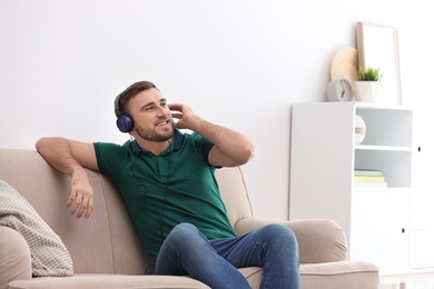 Young man in headphones enjoying music on sofa at home