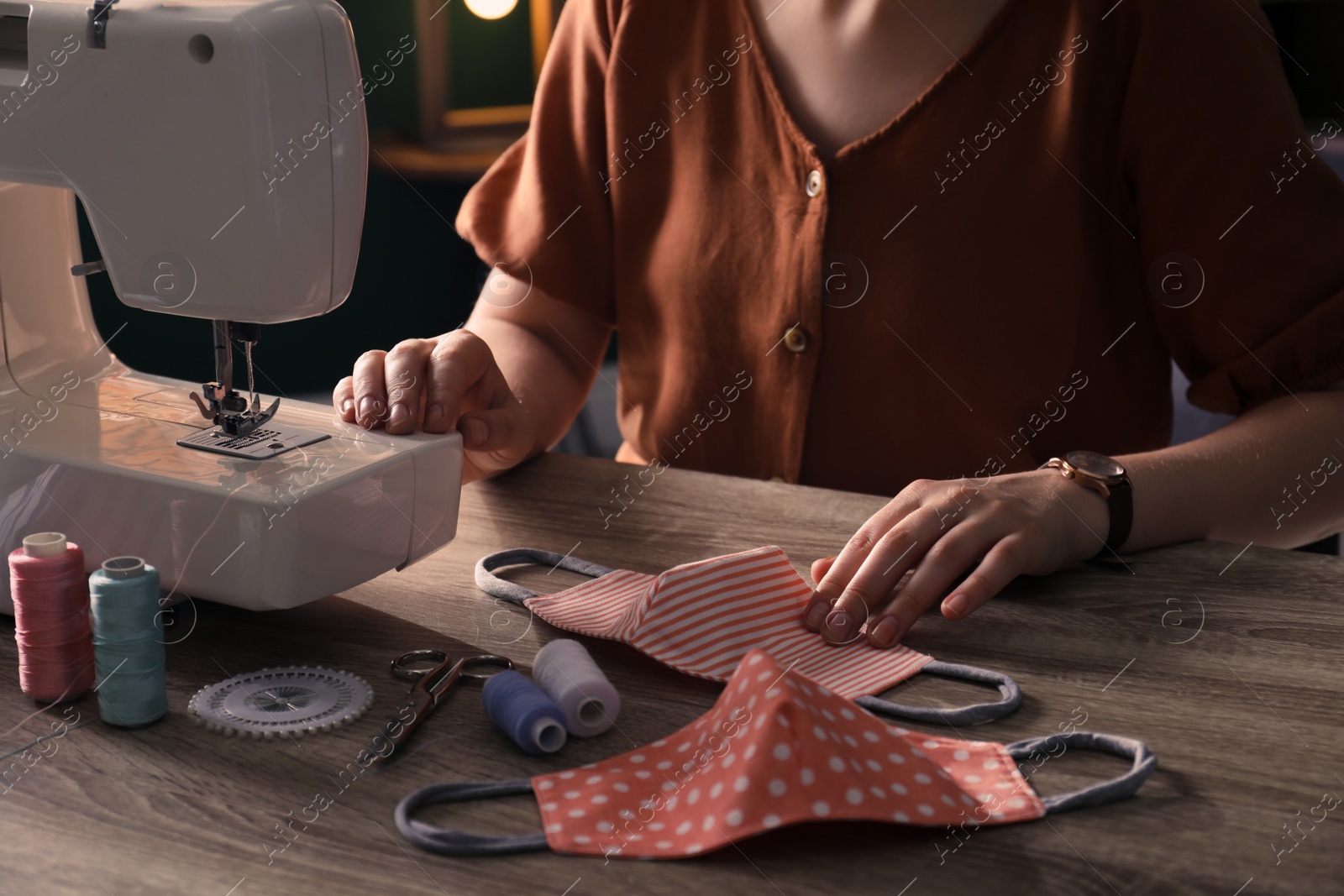 Photo of Woman sewing cloth protective mask with machine at table indoors, closeup