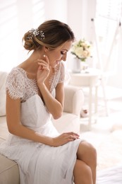 Gorgeous bride in beautiful wedding dress sitting on sofa in room