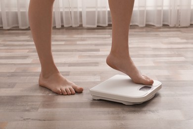 Photo of Woman stepping on floor scales indoors, closeup. Weight control