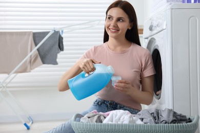 Photo of Woman pouring fabric softener from bottle into cap near washing machine in bathroom, space for text