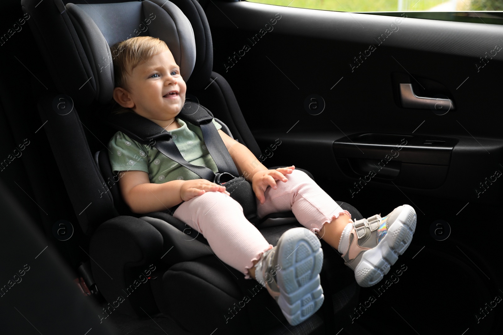 Photo of Cute little girl sitting in child safety seat inside car