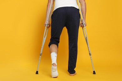 Photo of Man with injured leg using crutches on yellow background, closeup