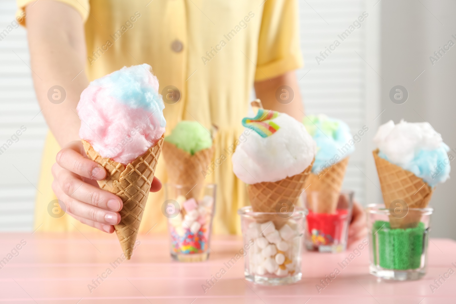 Photo of Woman holding waffle cone with cotton candy indoors, closeup