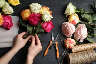 Photo of Woman making luxury bouquet of fresh roses at black table, top view