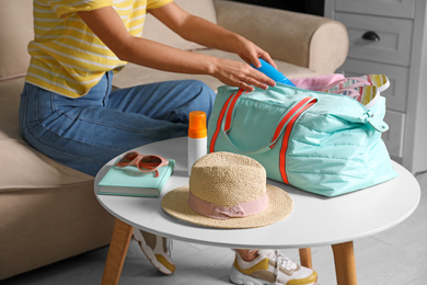 Woman putting items for vacation in bag indoors, closeup