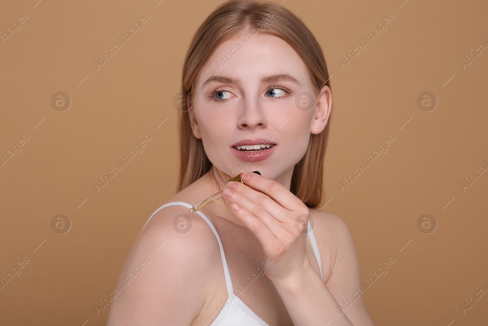 Photo of Beautiful young woman applying essential oil onto shoulder on brown background