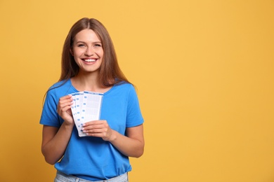Photo of Portrait of happy young woman with lottery tickets on yellow background, space for text