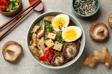 Photo of Bowl of delicious ramen and ingredients on grey table, flat lay. Noodle soup