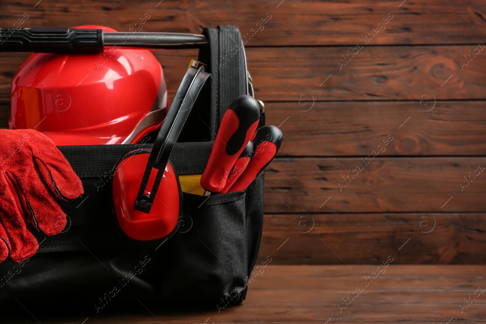 Photo of Black bag with construction tools on table against wooden background, space for text