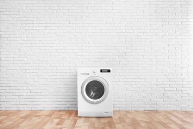 Modern washing machine near brick wall in empty laundry room