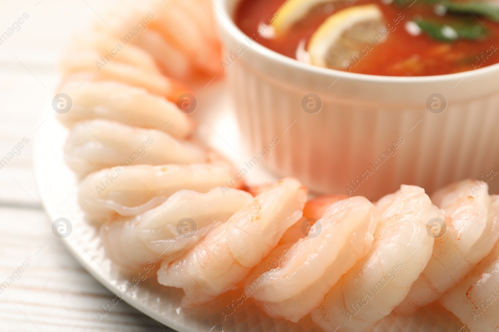 Photo of Tasty boiled shrimps with cocktail sauce and lemon on white wooden table, closeup