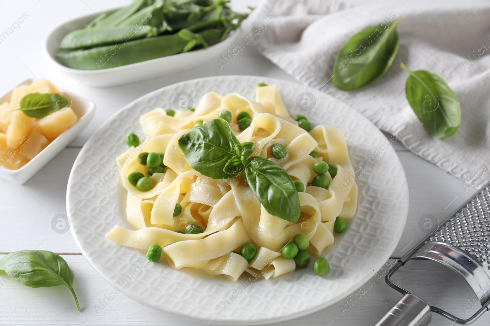 Photo of Delicious pasta with green peas and fresh basil on white wooden table