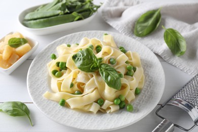 Photo of Delicious pasta with green peas and fresh basil on white wooden table