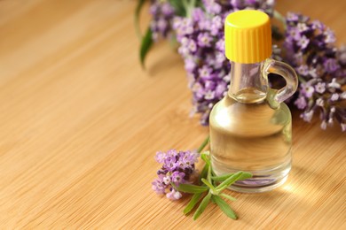 Photo of Bottle of natural essential oil and lavender flowers on wooden table, closeup. Space for text