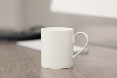 Photo of White ceramic mug and computer on wooden table at workplace