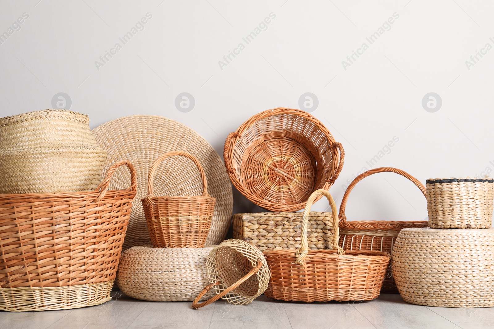 Photo of Many different wicker baskets made of natural material on floor near light wall