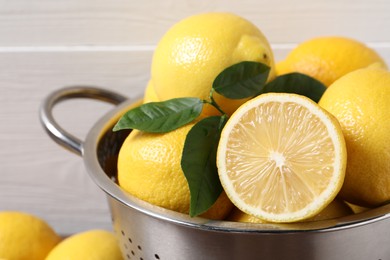 Photo of Fresh lemons and green leaves in colander, closeup