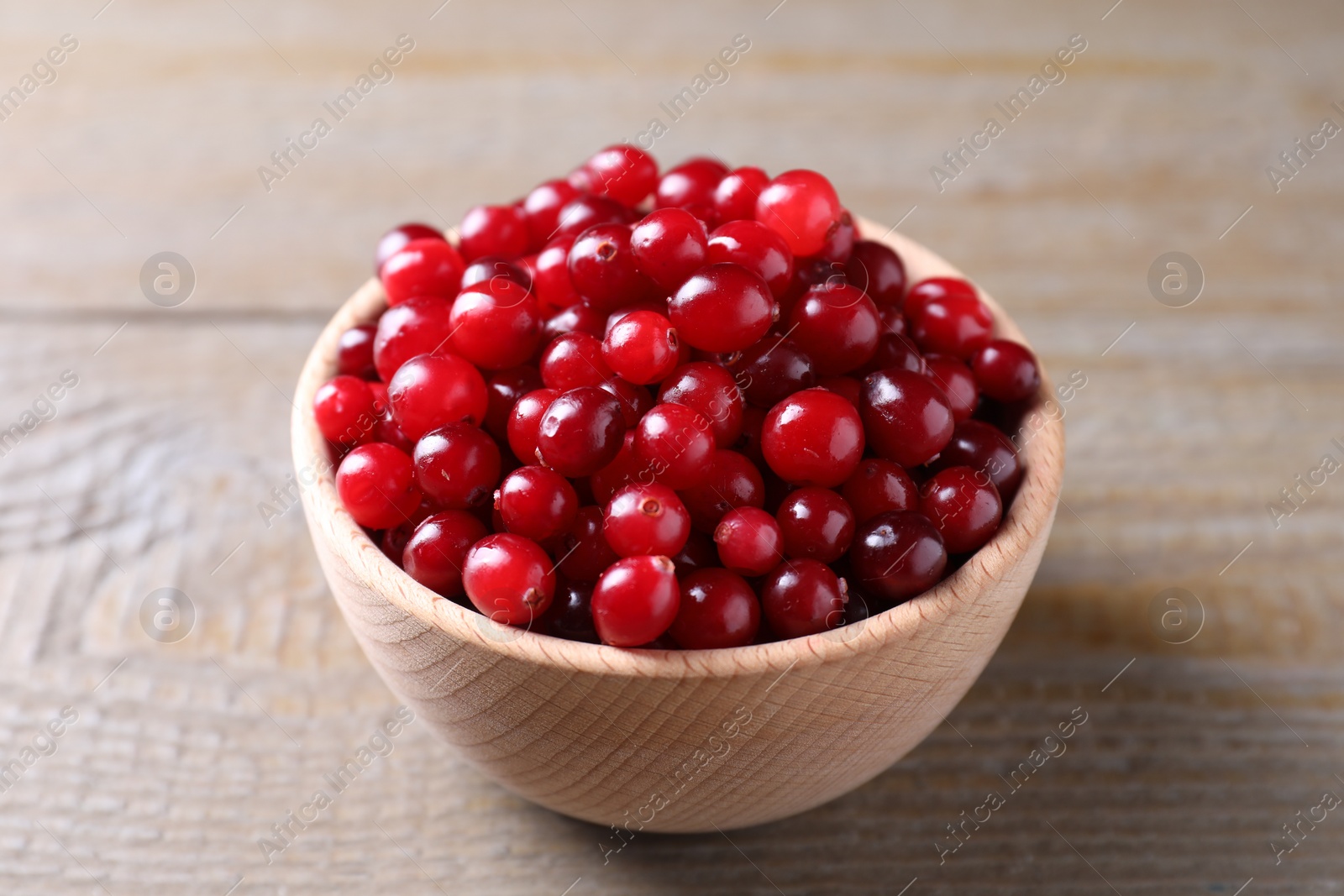 Photo of Fresh ripe cranberries in bowl on wooden table, closeup