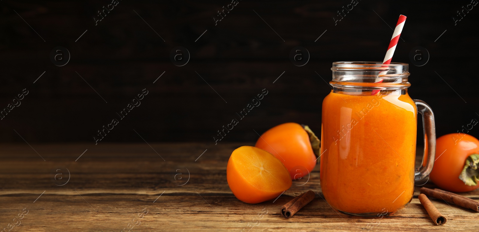 Image of Tasty persimmon smoothie with cinnamon on wooden table against dark background, space for text. Banner design